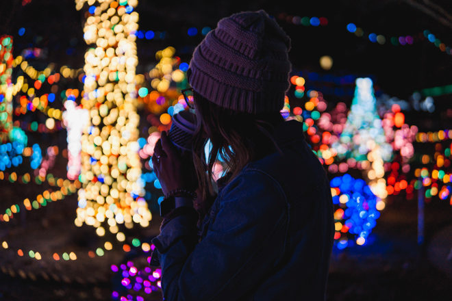 Woman sipping hot coffee while looking at christmas lights display